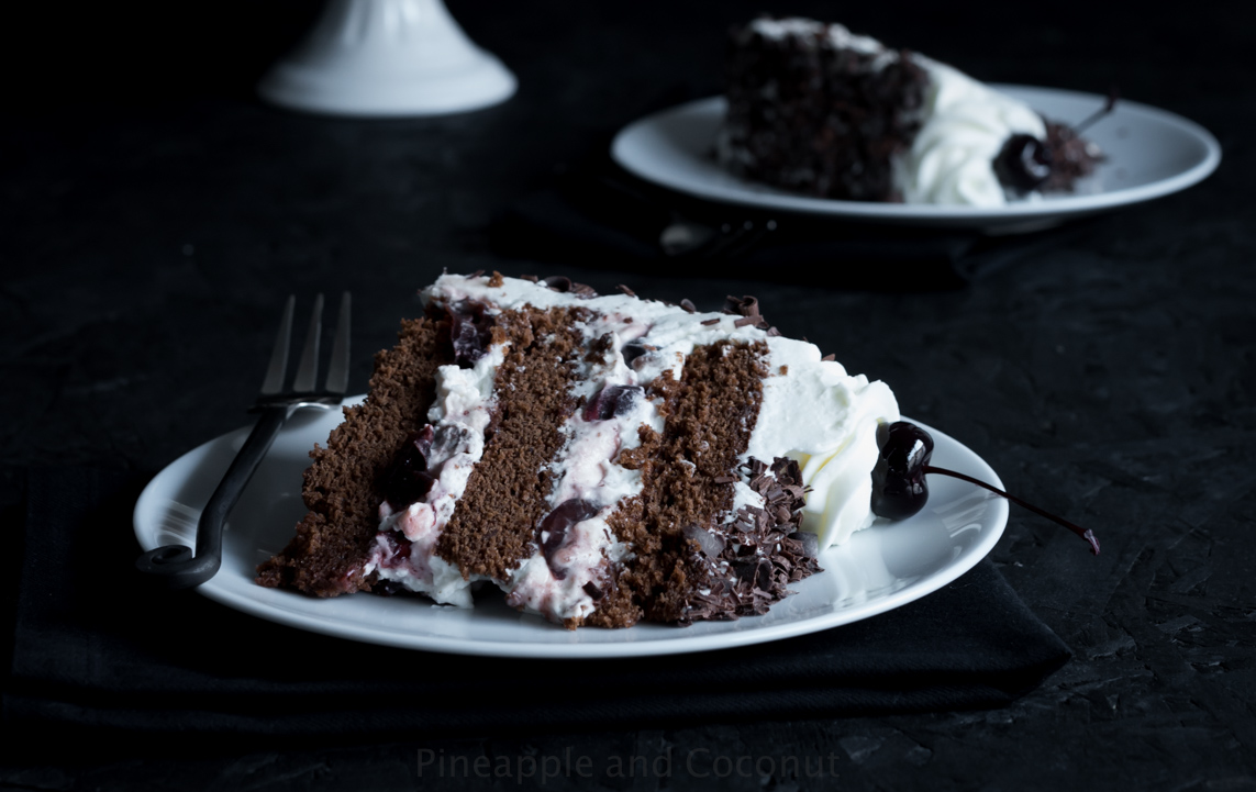 slice of chocolate layer cake on white plate, cake filled with whipped cream and cherries, chocolate curls, fork