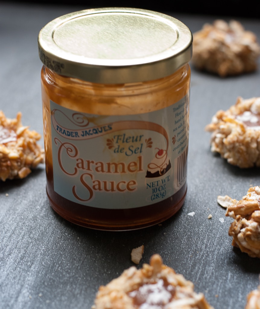 Jar of Trade Joe's salted caramel sauce with pretzel thumbprint cookies filled with caramel sprinkled with salt