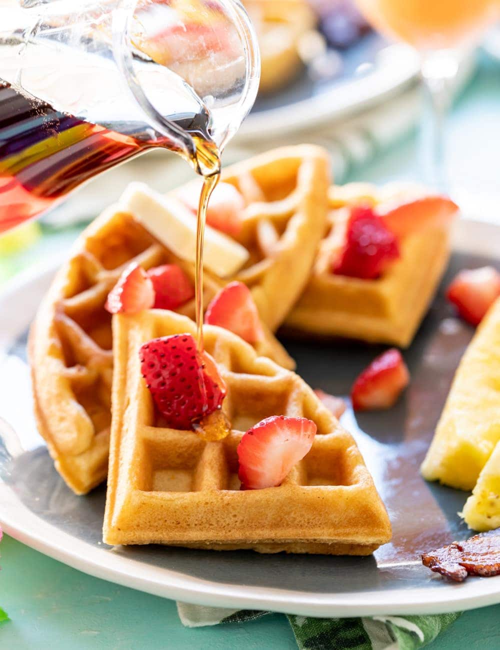 syrup being poured onto a coconut mochi waffle, strawberry slices on waffle