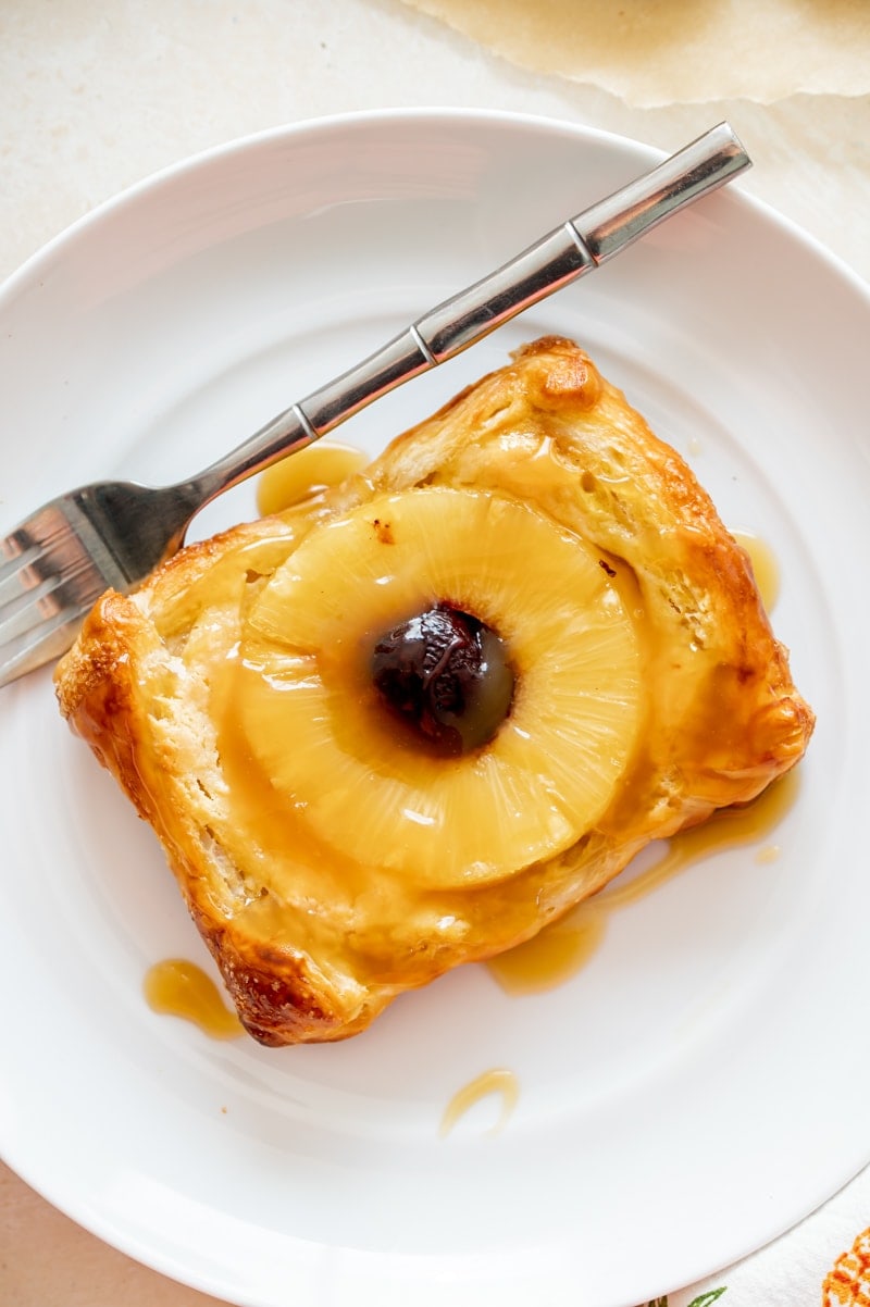 single puff pastry tart on white plate with fork, pineapple ring and cherry inside of tart www.pineappleandcoconut.com