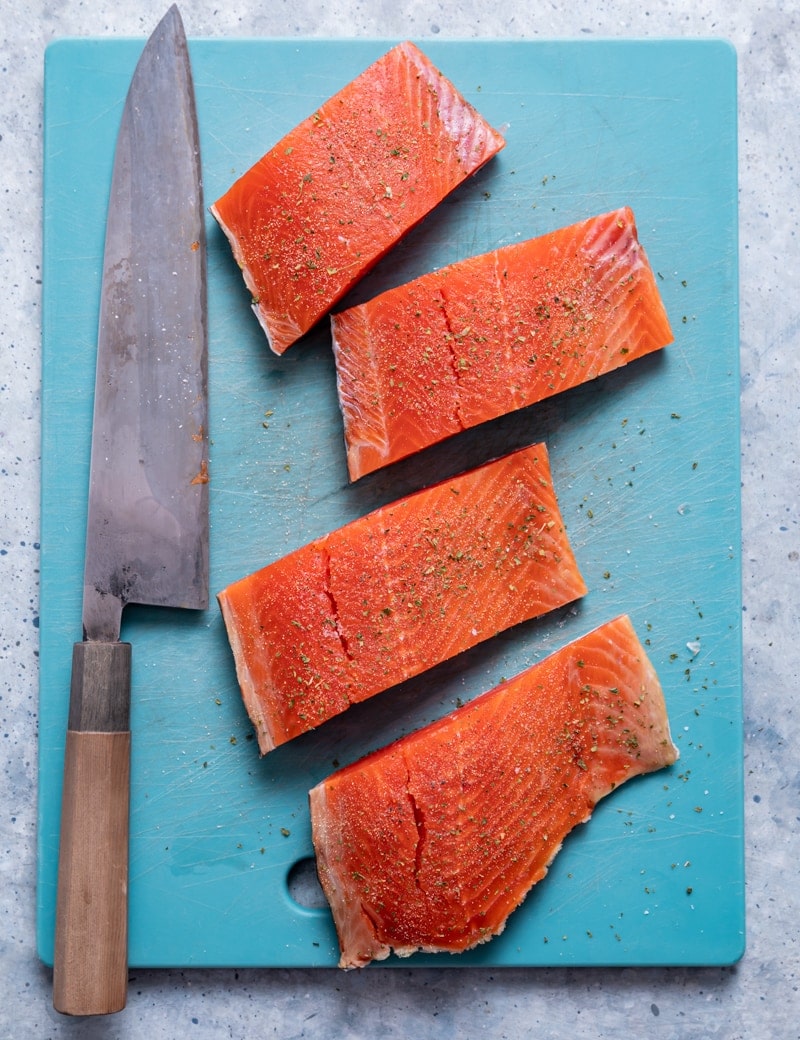 aqua cutting board with four salmon fillets, large knife