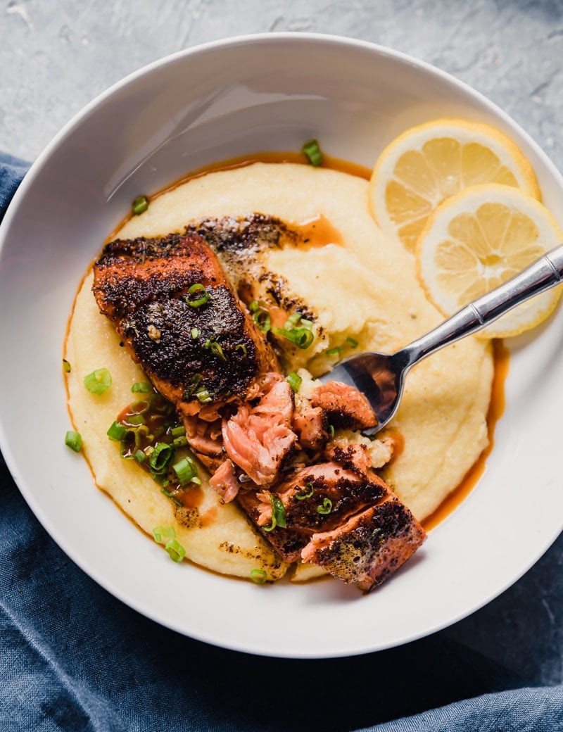 Closeup overhead food photo of wild alaskan sockeye salmon with cajun seasonings served over creamy grits with lemon and hot sauce