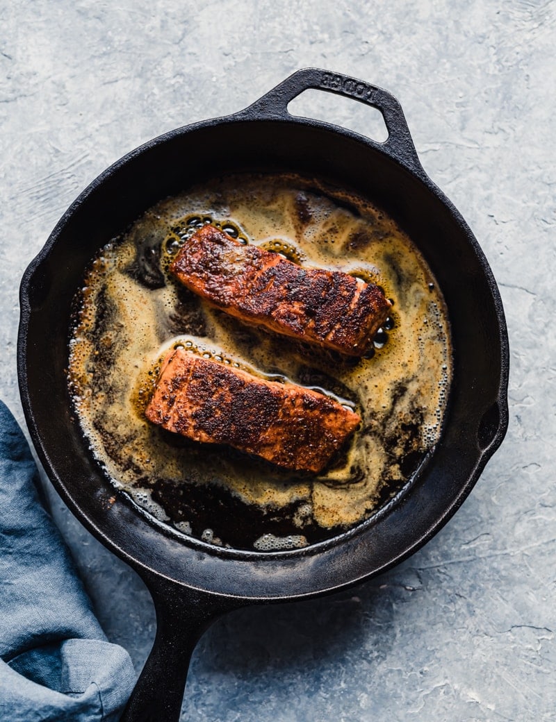 two cooked wild sockeye salmon fillets in a cast iron pan with sauce