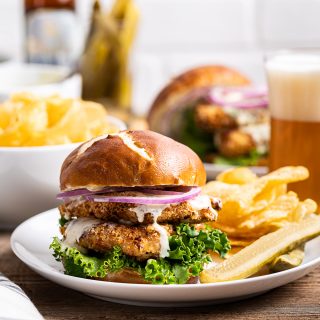 chicken schnitzel sandwiches on pretzel bun with green lettuce red onion kettle chips pickles and glass of beer