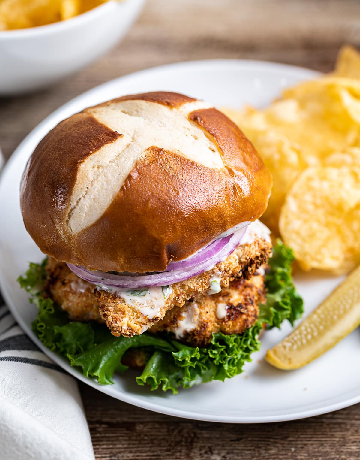 chicken schnitzel sandwich on a white plate with potato chips and pickle