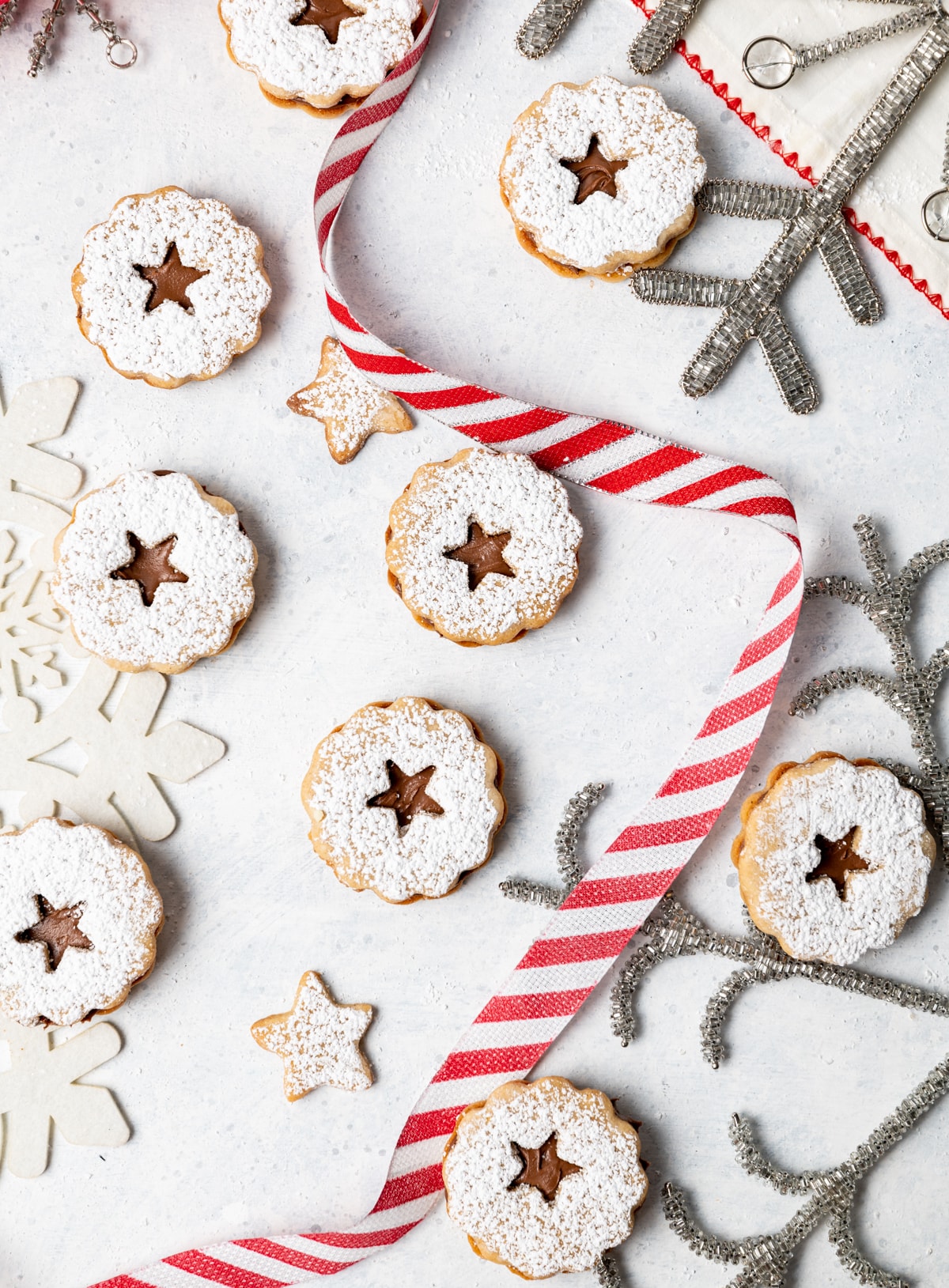 chocolate filled sandwich cookies on a white surface with red and white striped ribbon and silver snowflakes