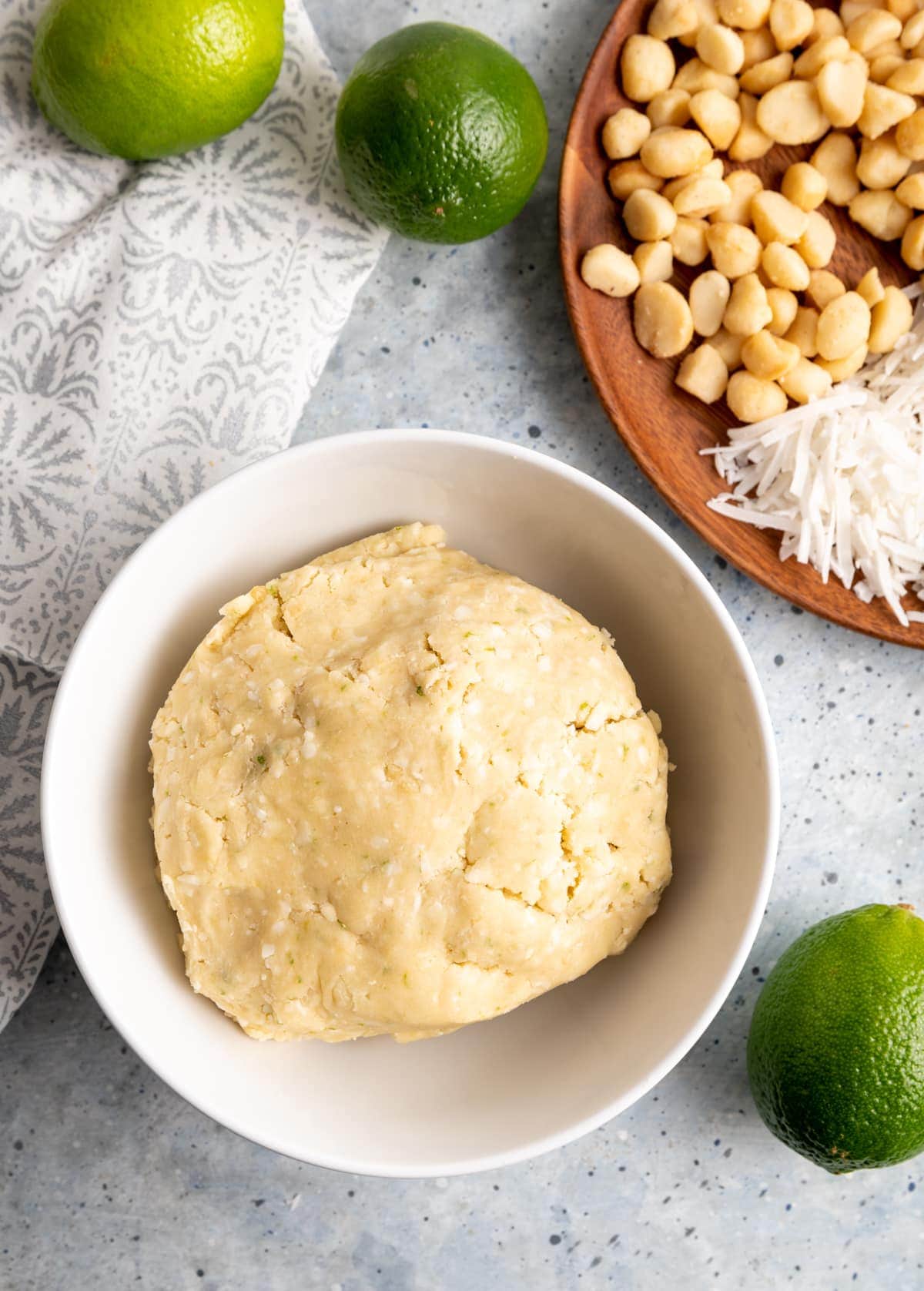 cookie dough in a bowl, limes, plate of macadamia nuts and shredded coconut