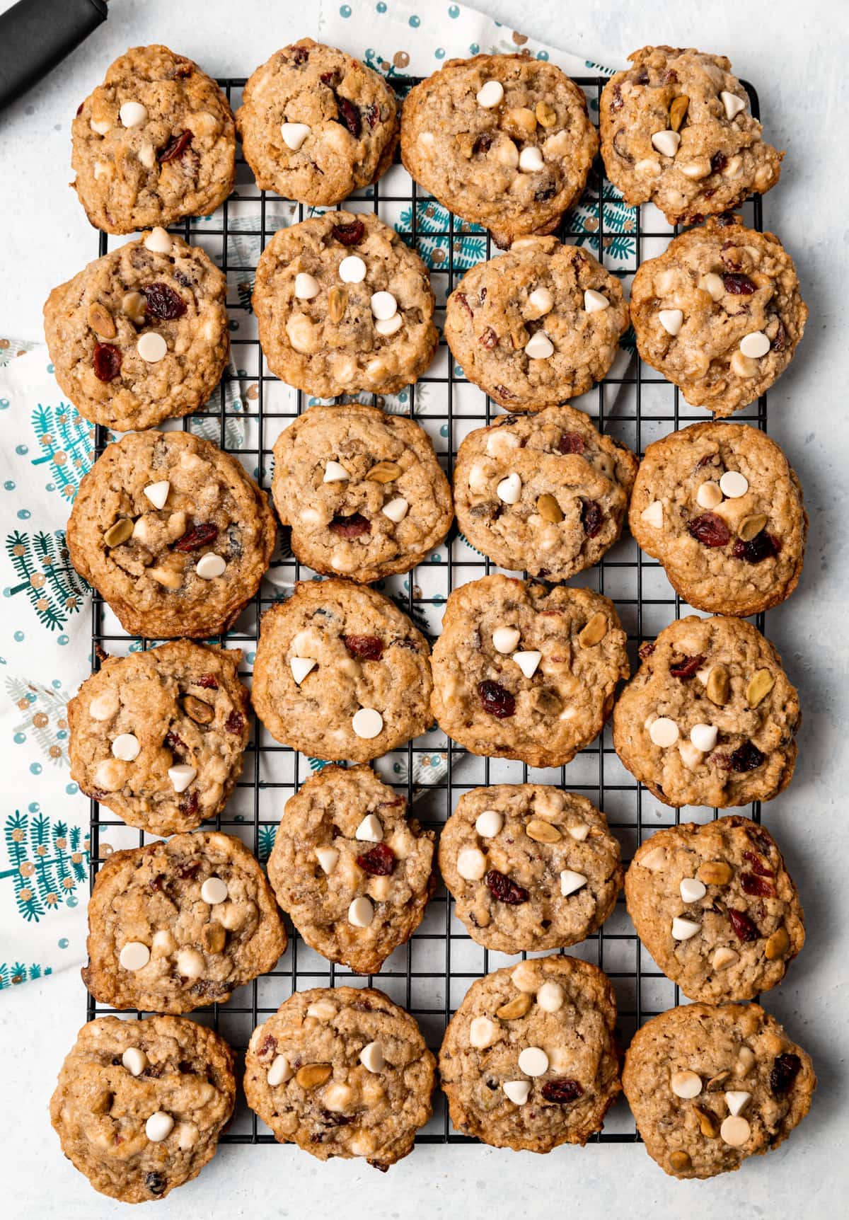 wire rack filled with oatmeal cookies with white chocolate chips cranberries and pistachios white napkin with green trees