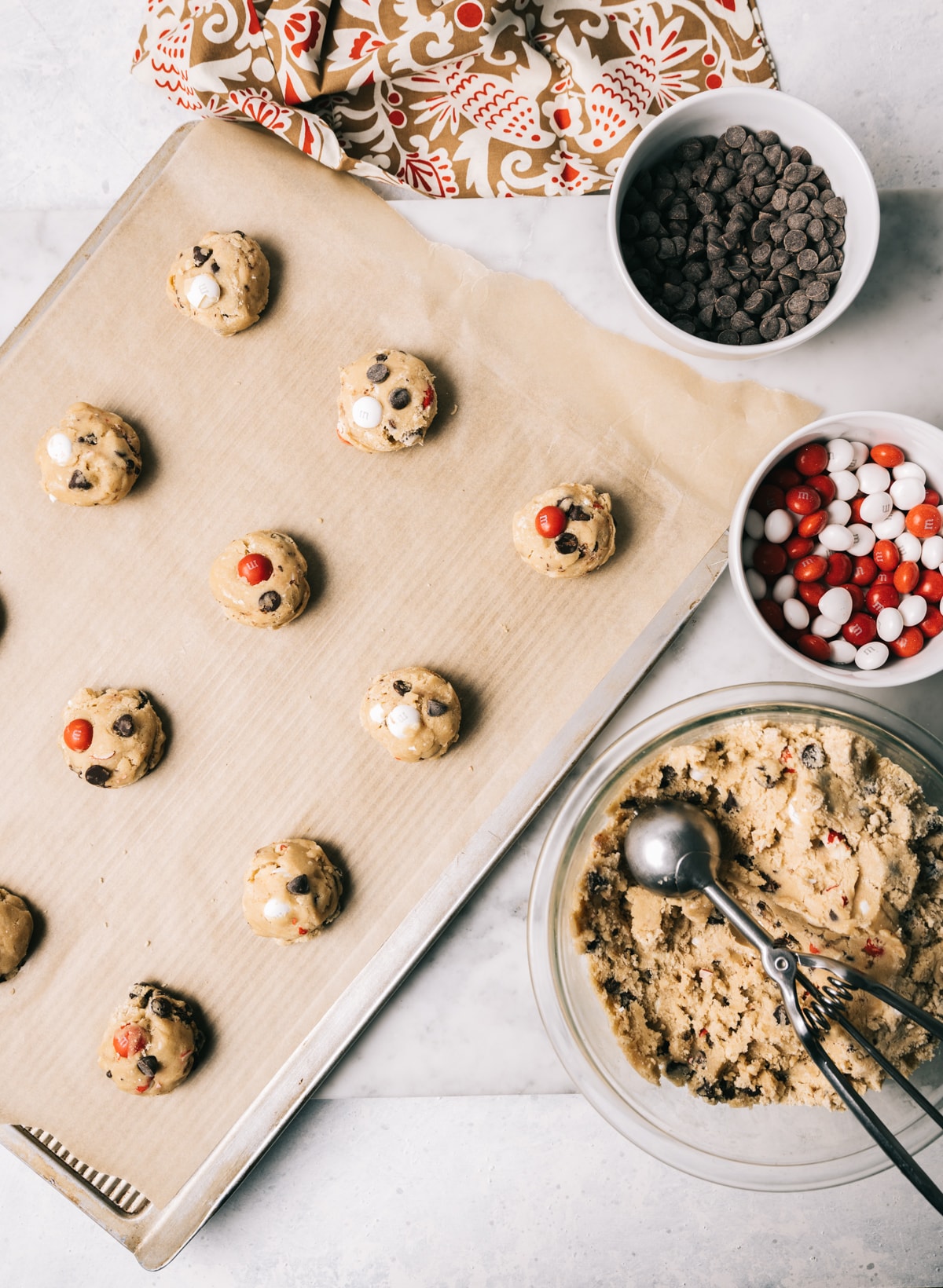 chocolate chip cookie dough balls on a baking tray with parchment paper bowl of cookie dough bowl of M&Ms bowl of chocolate chips