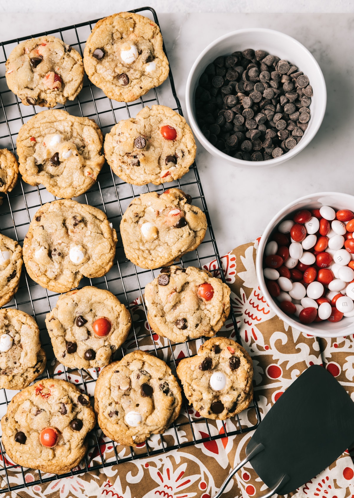 chocolate chip cookies with red and white M&Ms on a wire rack bowl of chocolate chips bowl of M&Ms