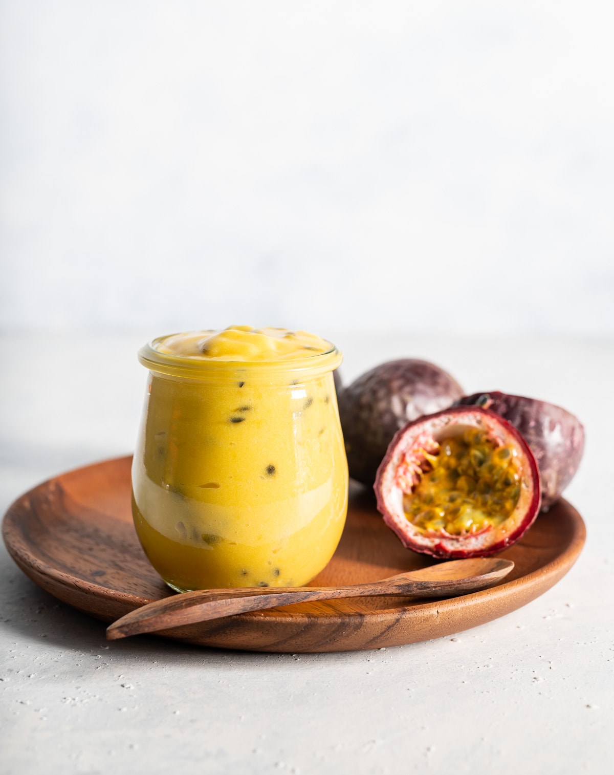 yellow passion fruit curd in a jar with fresh passion fruits cut in half brown plate