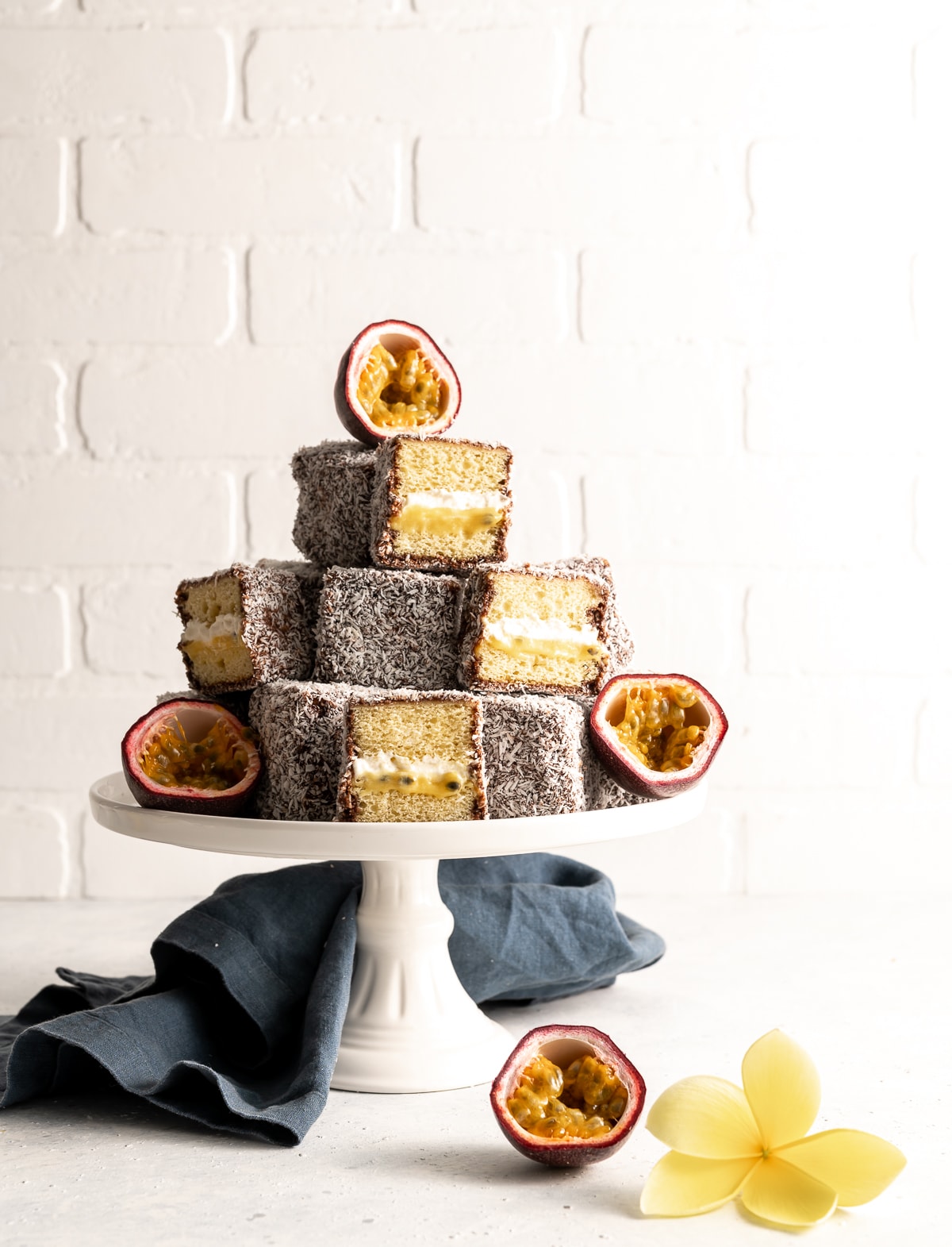 tower of lamingtons on a cake plate some whole some cut in half fresh passion fruit cut in half