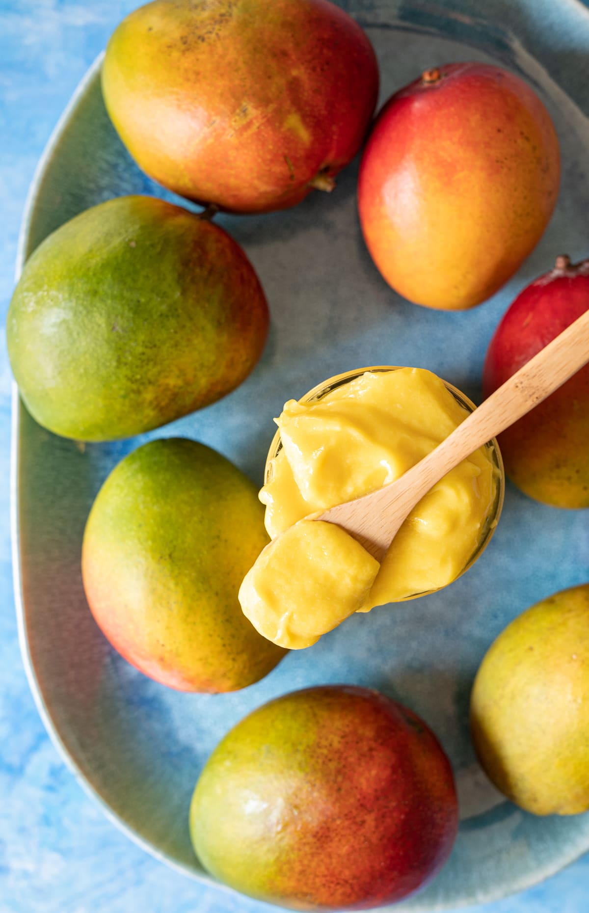 yellow mango curd in a jar on a blue plate with whole mangoes