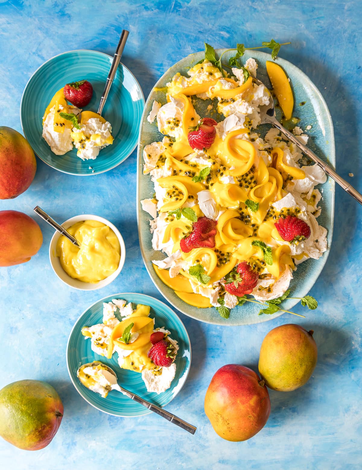 smashed pavlova on a blue platter with mangoes passion fruit and strawberries