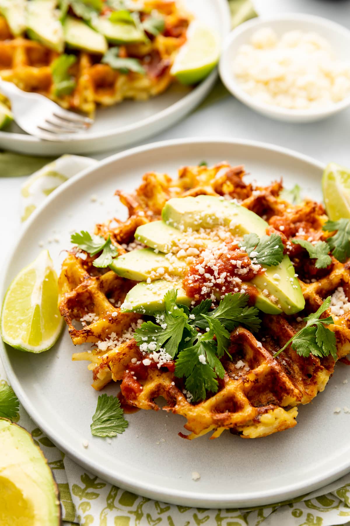 hash brown waffles on white plate with lime slices white crumbled cheese avocado slices cilantro