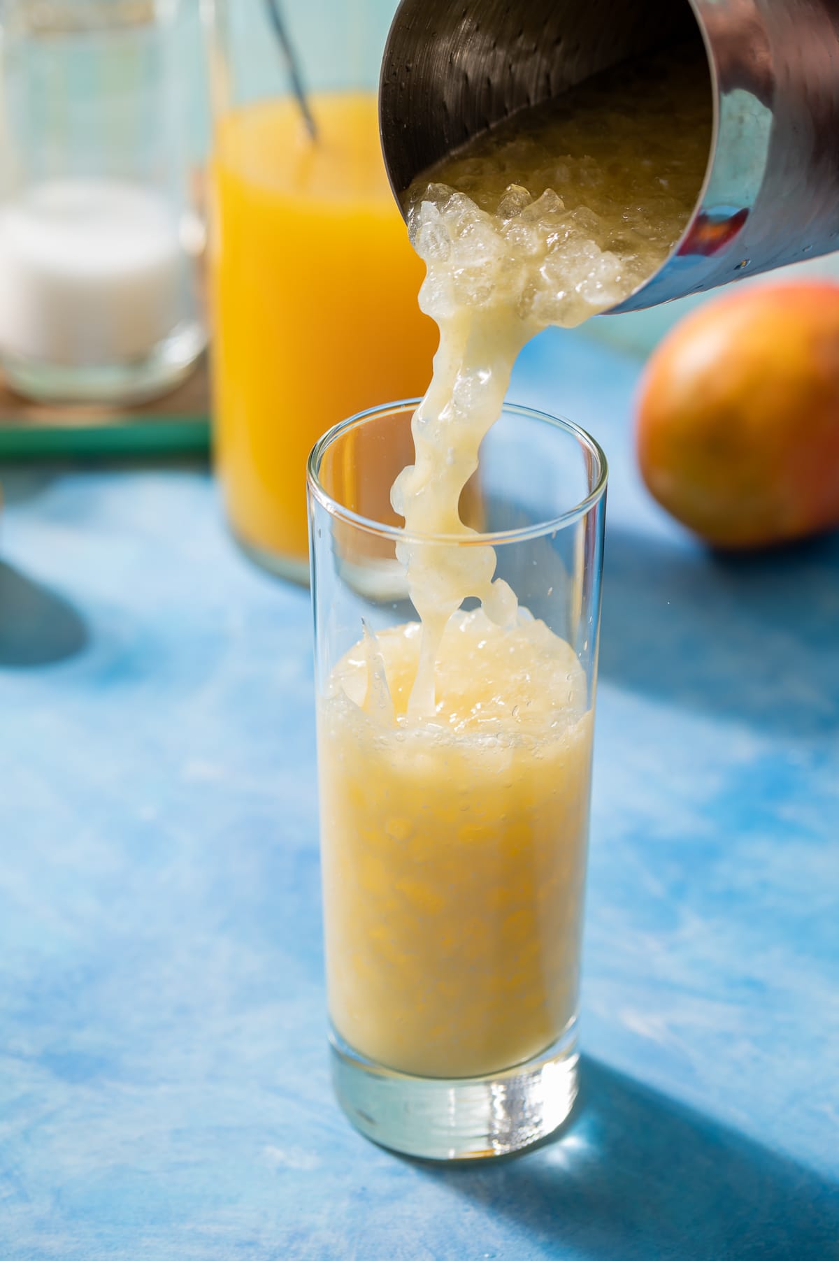 coconut mango lemonade being poured into a glass from a cocktail shaker with ice