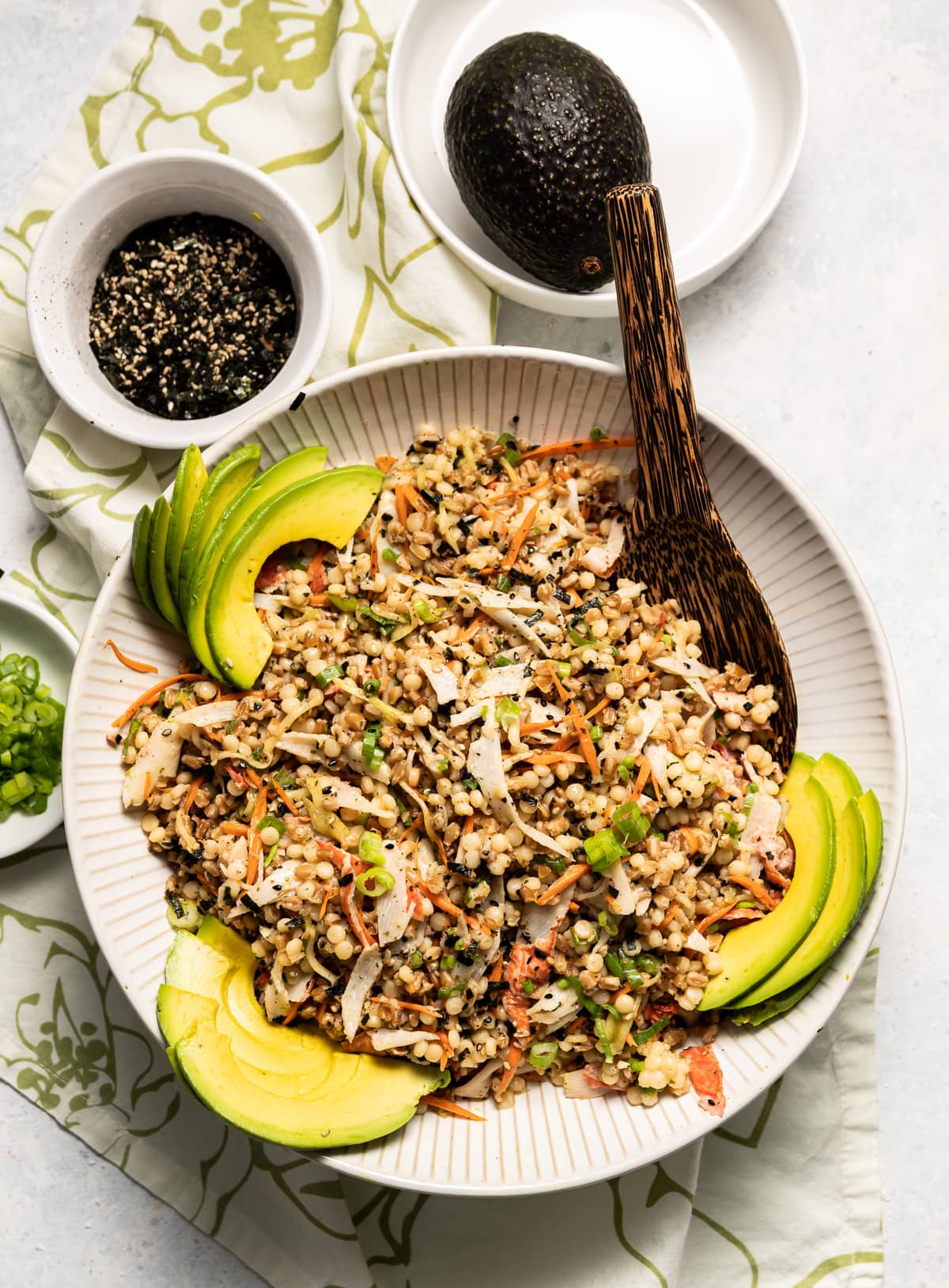 california roll salad with mixed grains and vegetables in white bowls bowl or green onion whole avocado bowl of seaweed seasoning