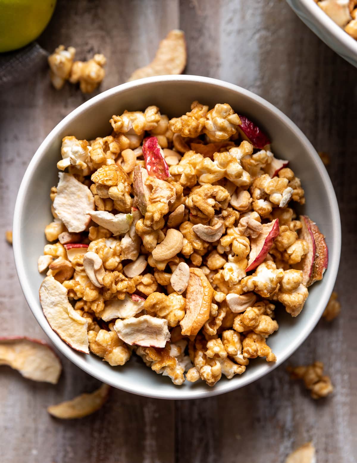 small light blue bowl filled with brown caramel popcorn red dried apple pieces and tan cashews