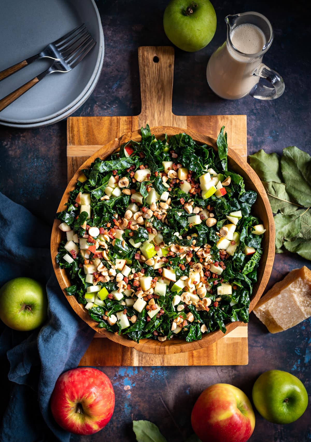 wooden bowl with kale salad topped with chopped apples and hazelnuts on a wooden cutting board whole apples 