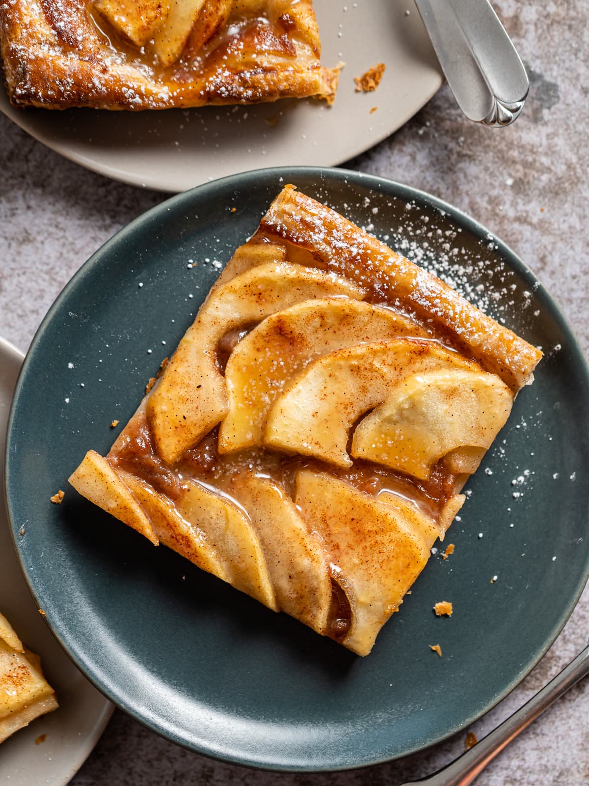 cut slice or puff pastry with apple slices on it on a dark gray plate