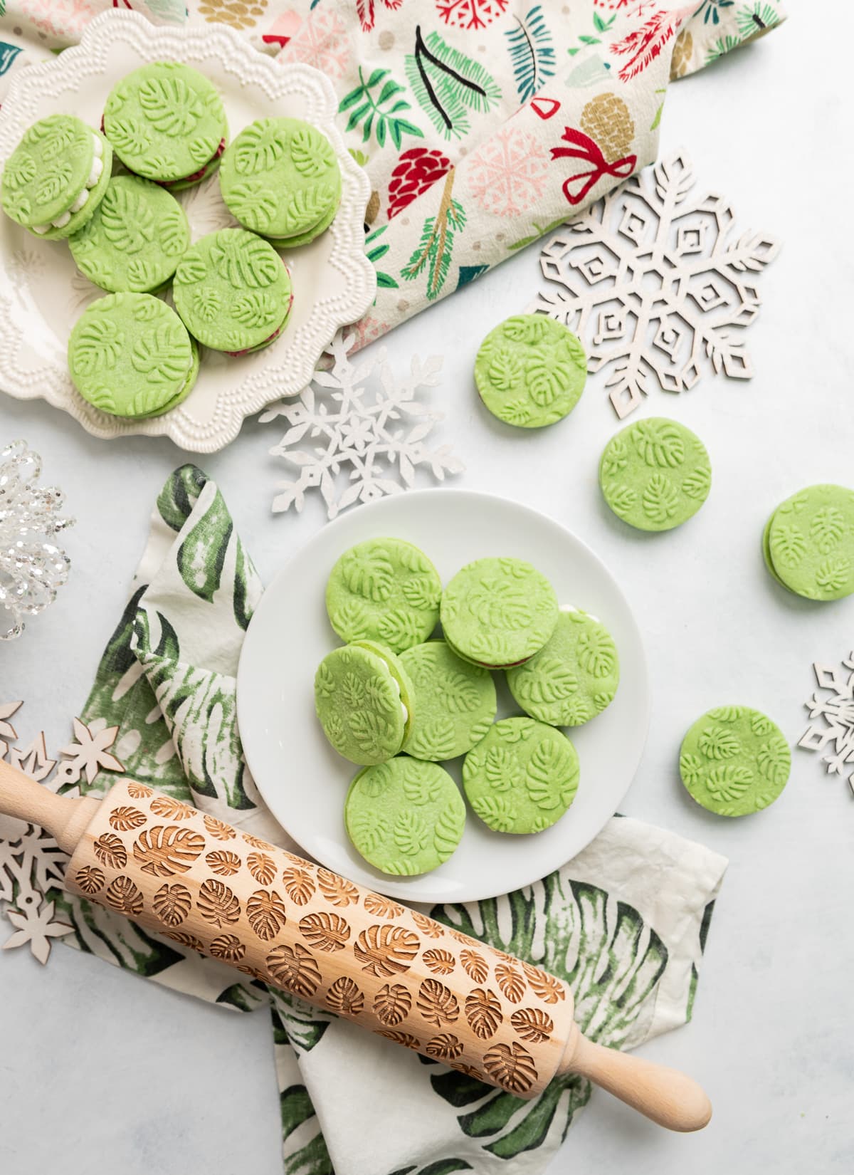 green pandan sandwich cookies with white and red buttercream filling and an embossed monstera leaf pattern on the cookies