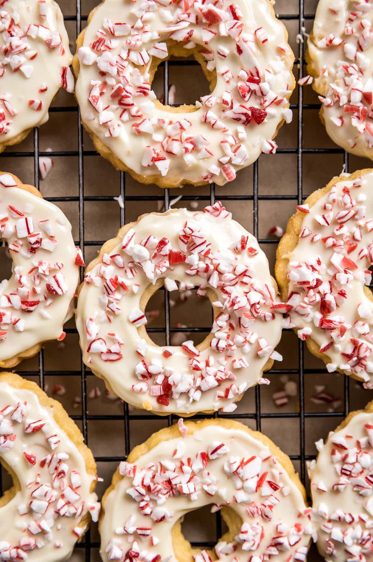 wreath shaped cookies with chite chocolate icing and peppermint bits on a wire rack