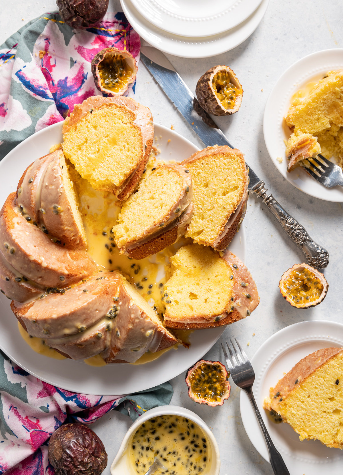 yellow passionfruit bundt cake sliced on a large white plate slices on smaller white plates pink and blue napkins whole and halved passion fruits