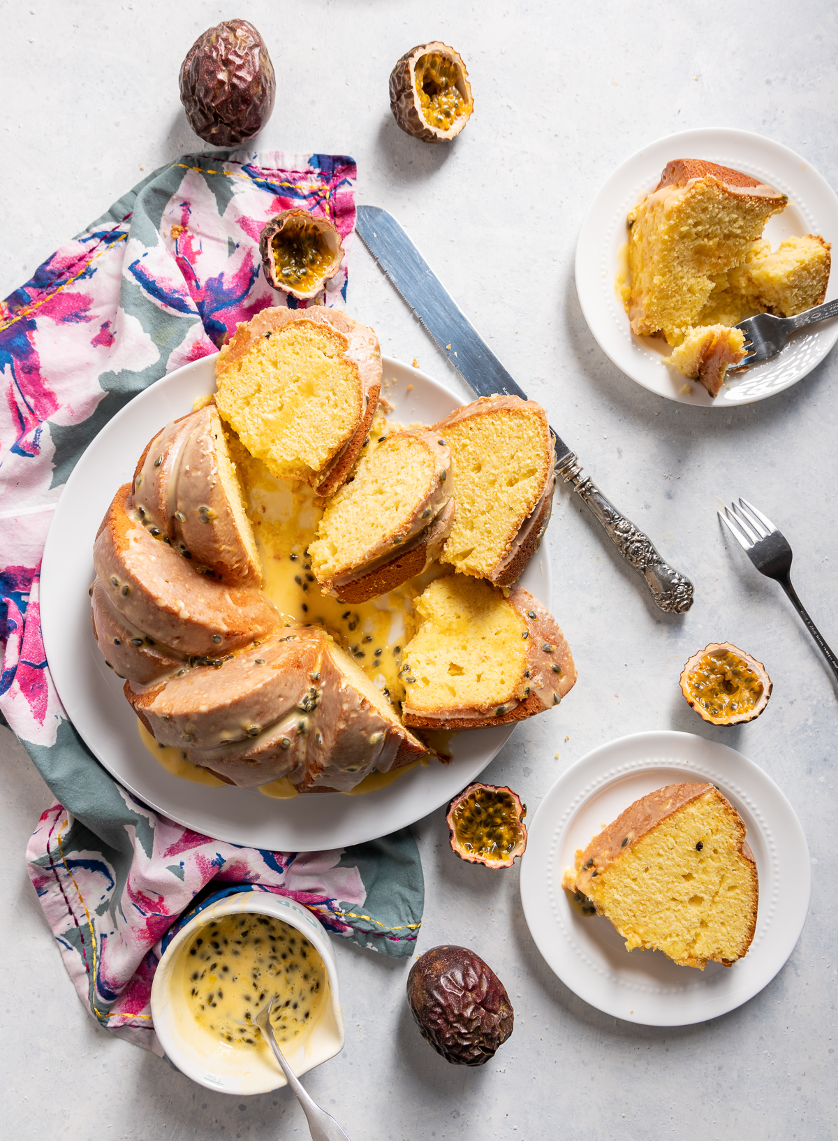 yellow passionfruit bundt cake sliced on a large white plate slices on smaller white plates pink and blue napkins whole and halved passion fruits