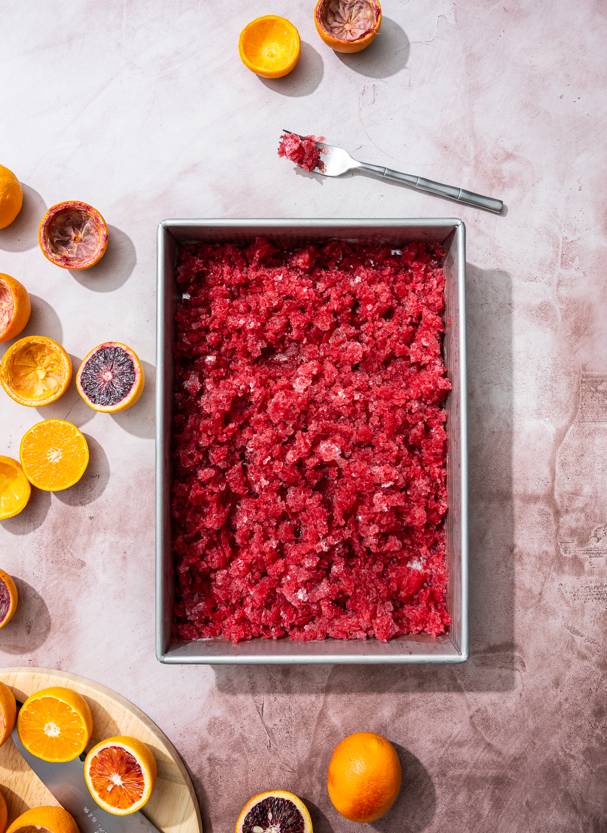 tray of reddish orange granita scraped up blood orange and tangerine slices fork