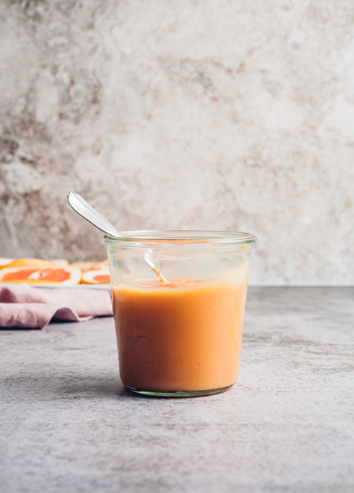 pinkish orange curd in glass jar with spoon plate of pink grapefruit slices pink napkin