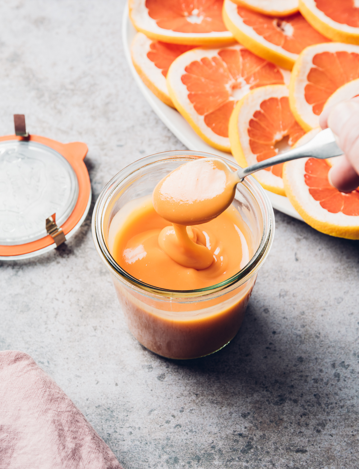 pinkish orange curd in glass jar with spoon plate of pink grapefruit slices pink napkin