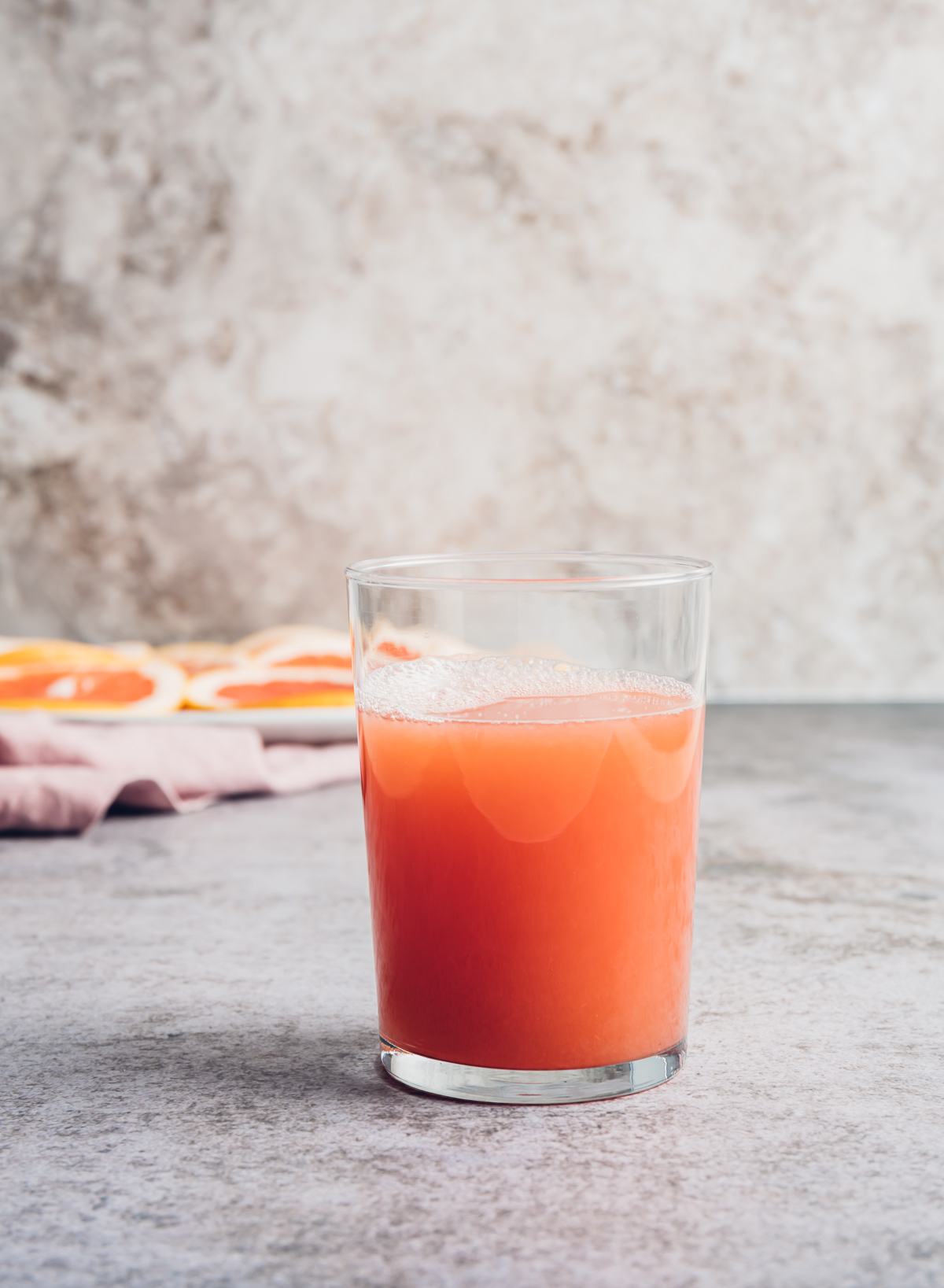 glass of pink grapefruit juice pink napkin white plate with pink grapefruit slices