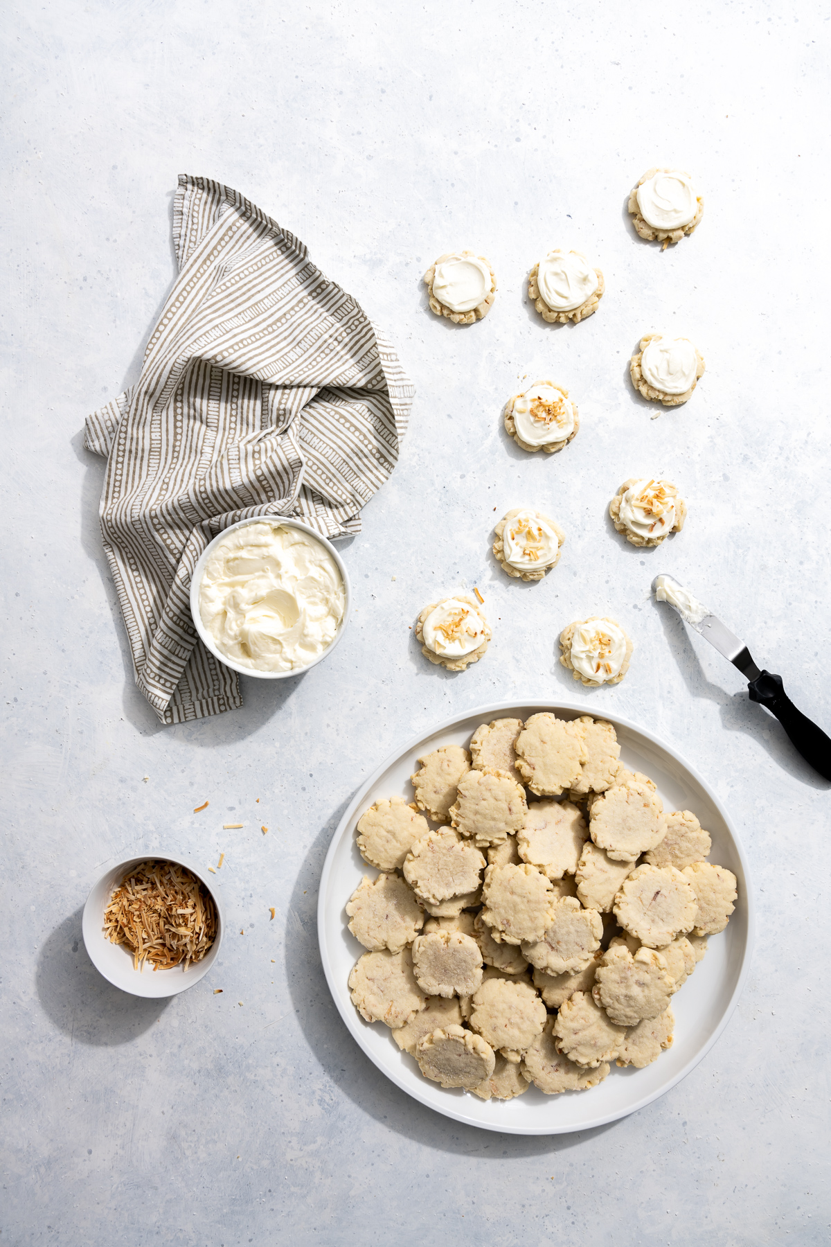 plate of coconut cookies bowl of coconut frosting bowl of toasted coconut fakes several cookies frosted spatula
