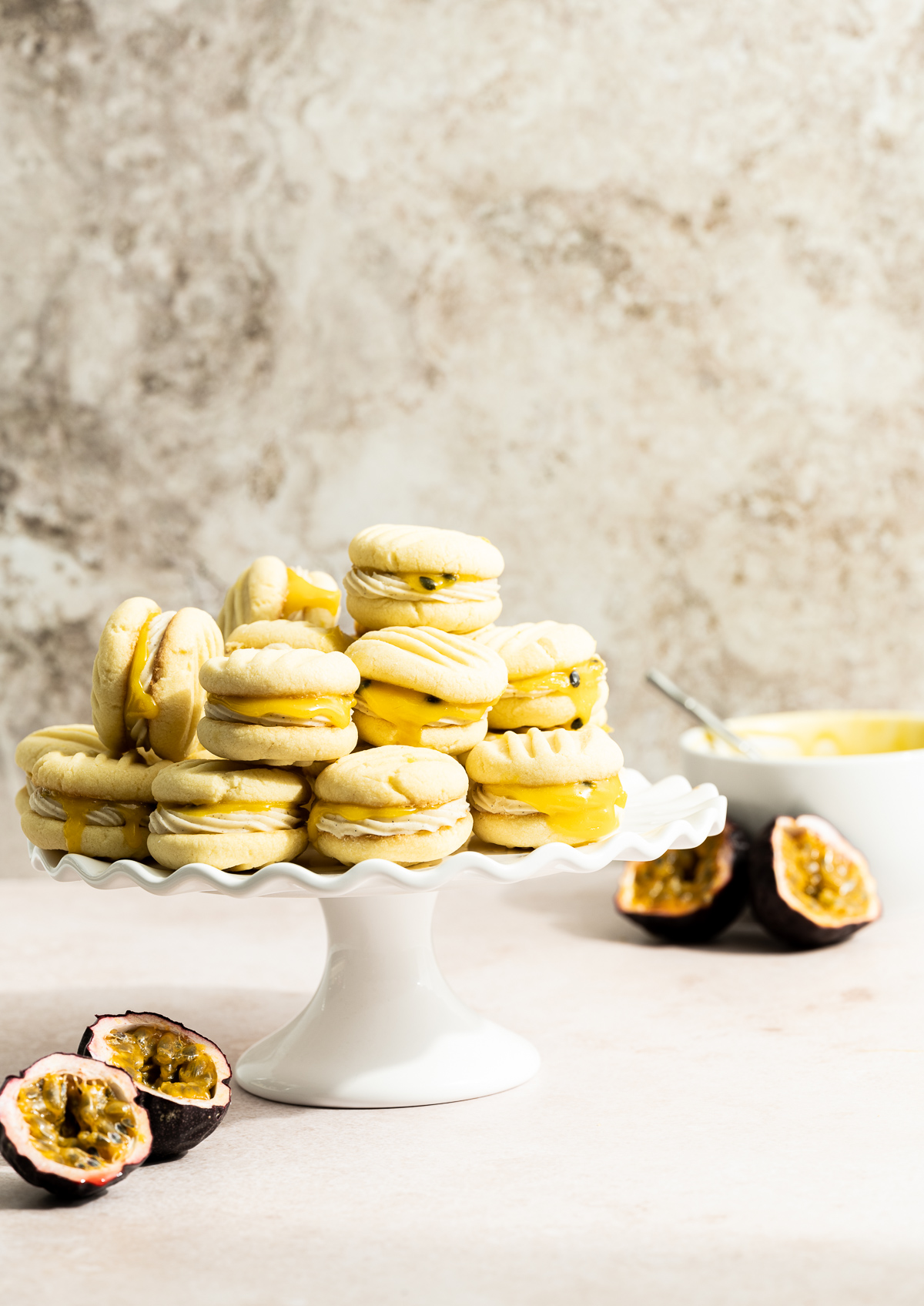 passionfruit sandwich cookies on a white cake plate bowl of passionfruit curd fresh passionfruit cut in half