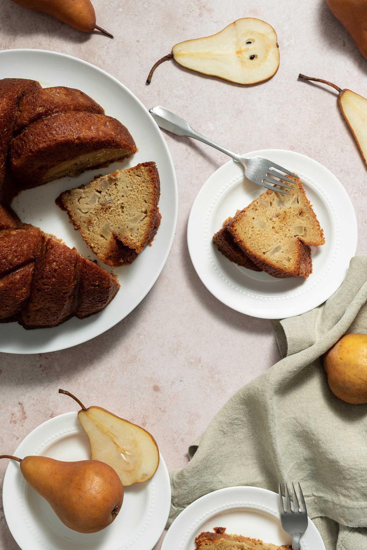 maple pear bundt cake on white plate with whole and sliced bosc pears slice of cake on plate fork