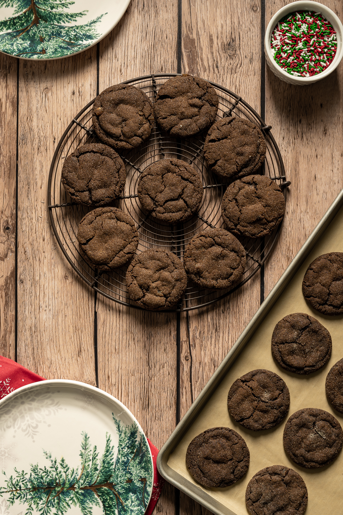 round chocolate cookies on a round wire tray bowl of red white and green sprinkles cookies on a baking sheet