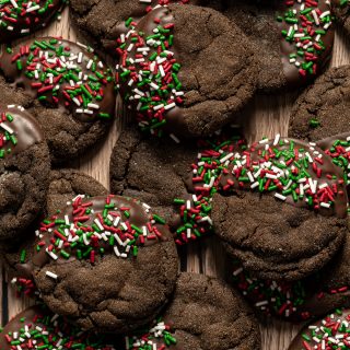 Round chocolate cookies half dipped in chocolate decorated with red white and green sprinkles