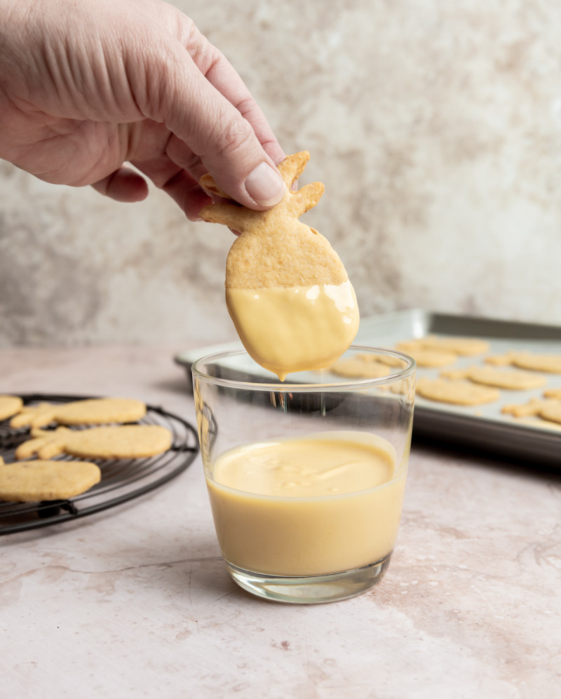 a pineapple shaped cookie being dipped in passionfruit chocolate