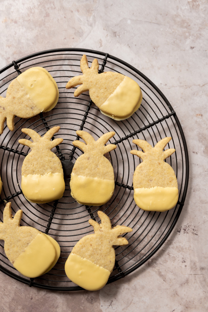 pineapple shaped cookies half dipped in passionfruit chocolate on a wire cooling rack