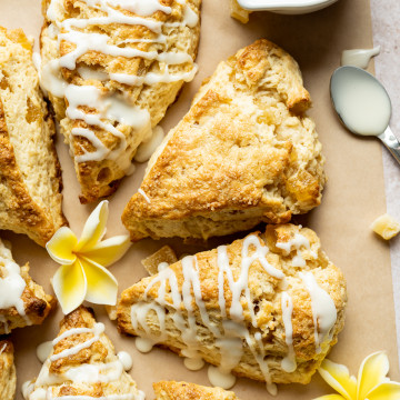 Cut pineapple scone wedges on brown parchment bowl of glaze spoon yellow plumerias