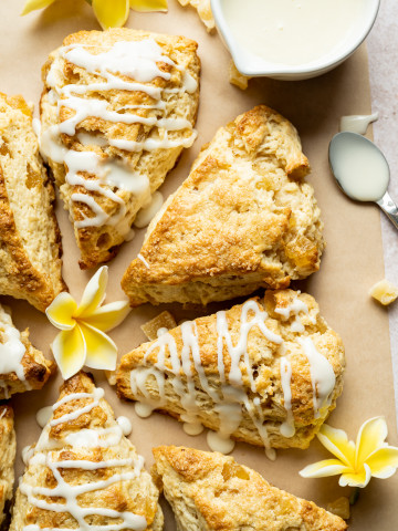 Cut pineapple scone wedges on brown parchment bowl of glaze spoon yellow plumerias