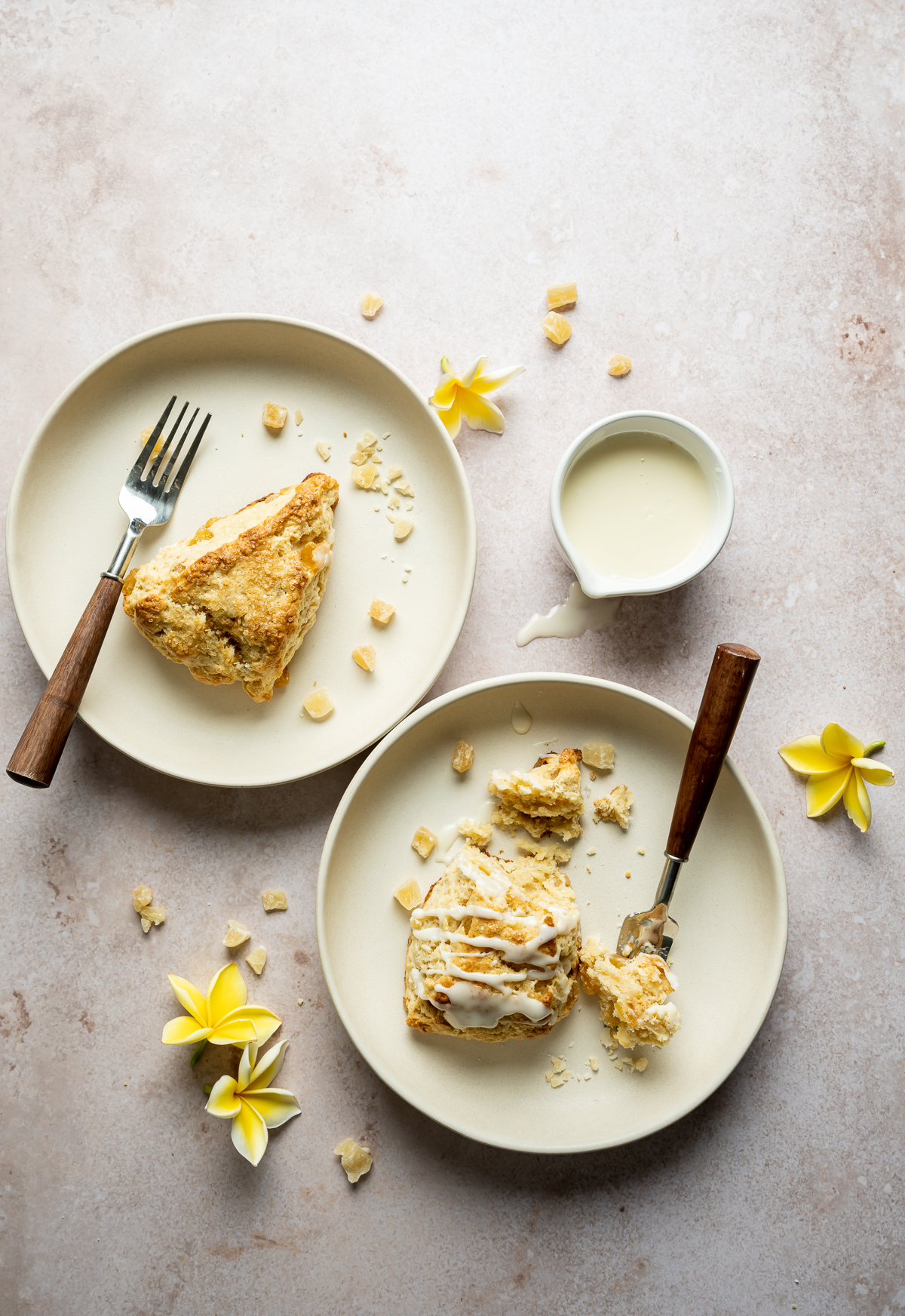 Cut scone wedges on beige plates with forks bowl of glaze spoon yellow plumerias