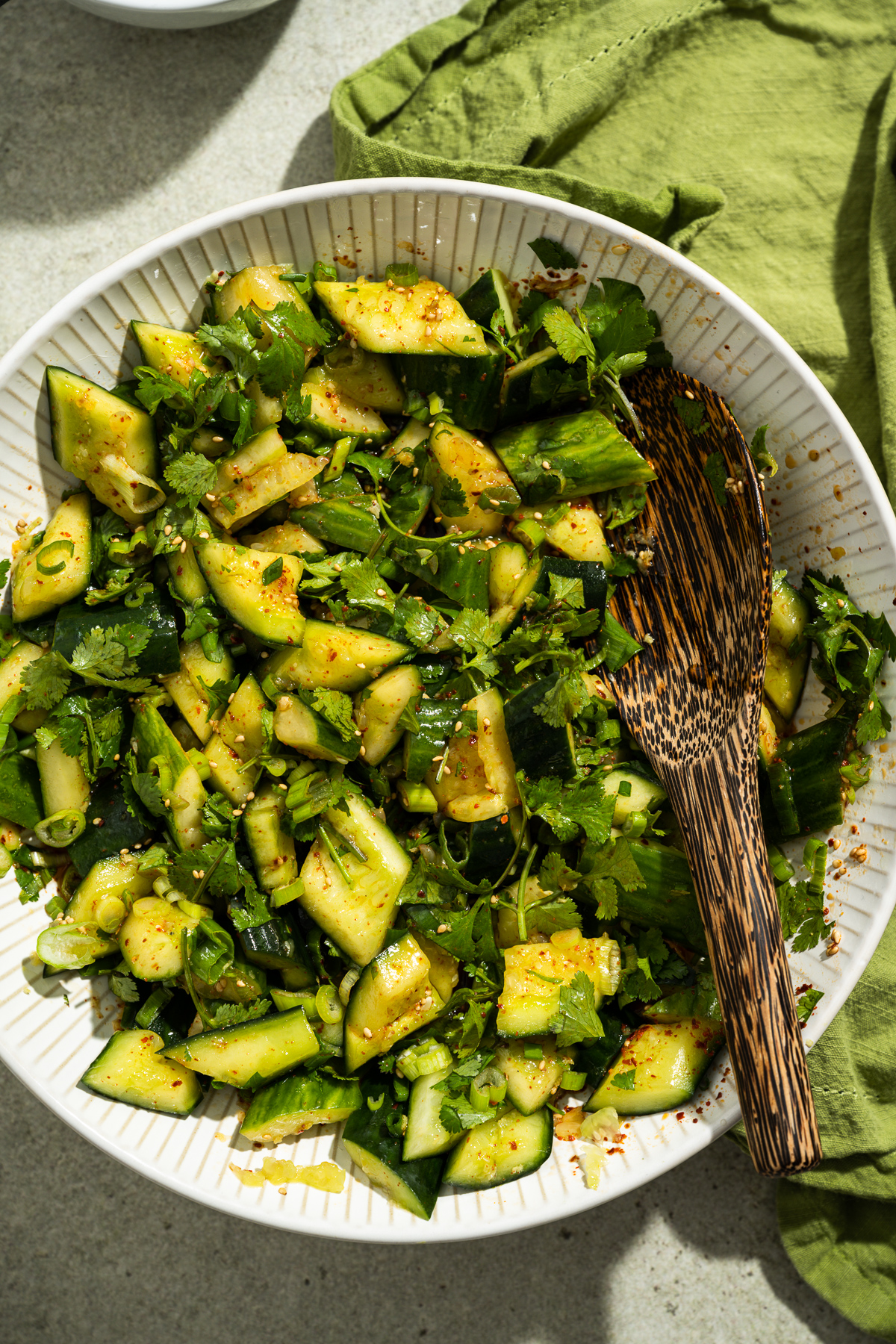 smashed cucumber salad in a white bowl green napkin wooden serving spoon