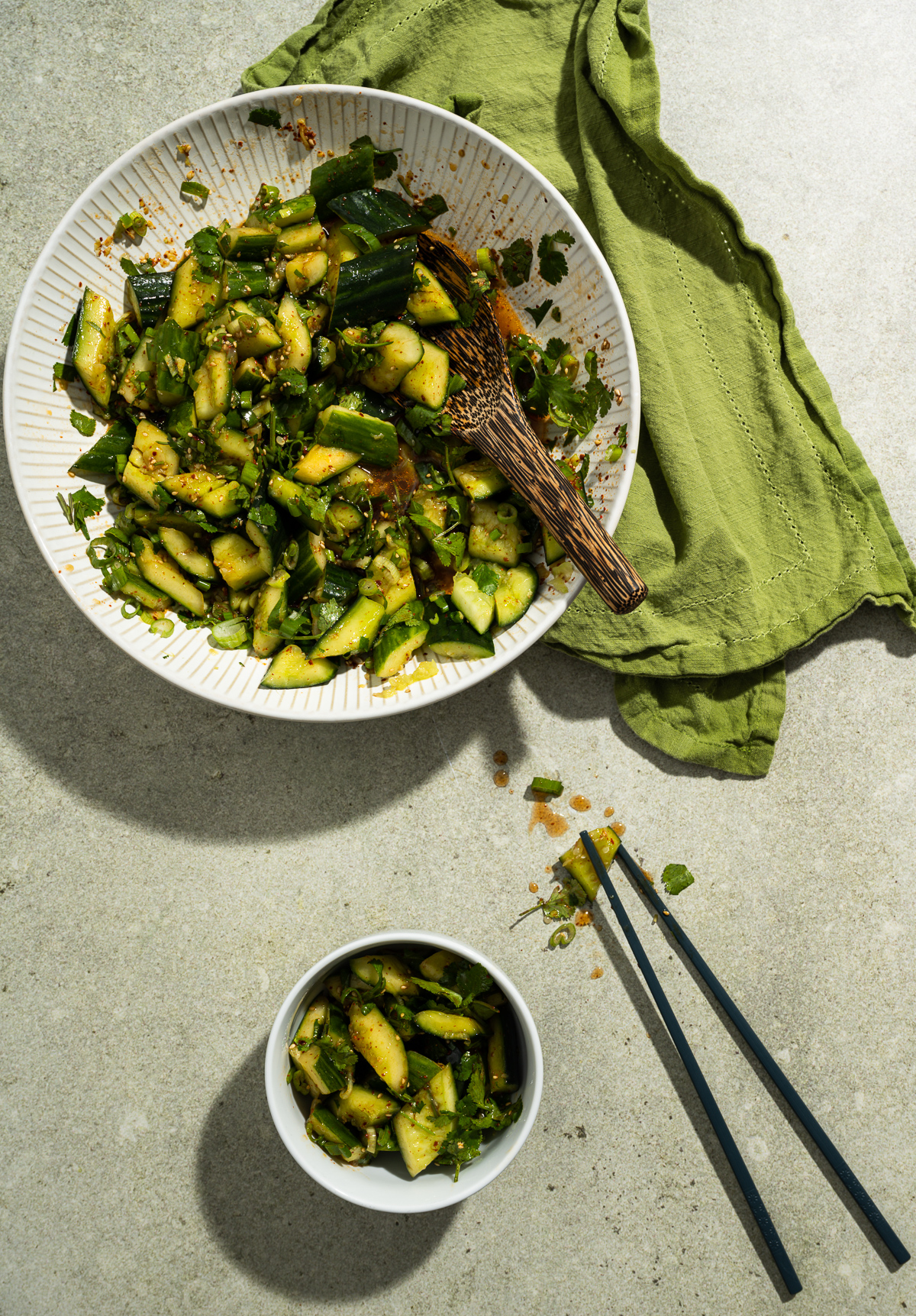 smashed cucumber salad in a white bowl green napkin wooden serving spoon