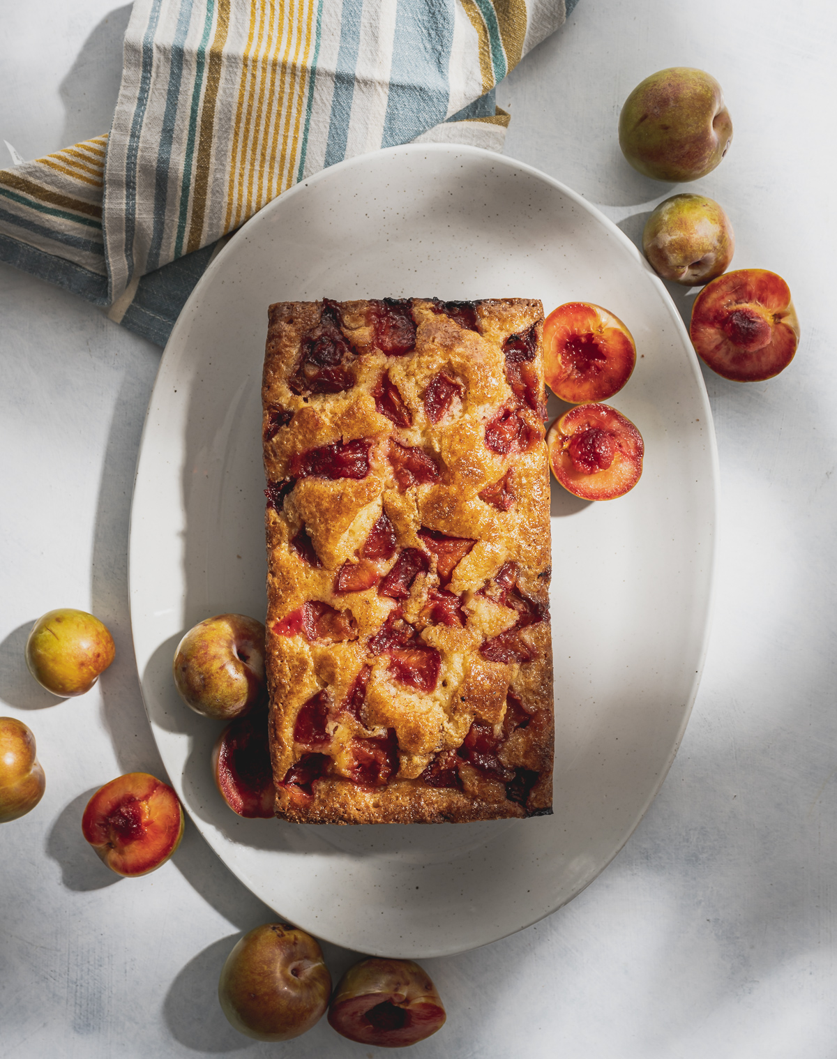 whole baked plum pound cake on speckled plate whole and halved plums blue and yellow striped napkin