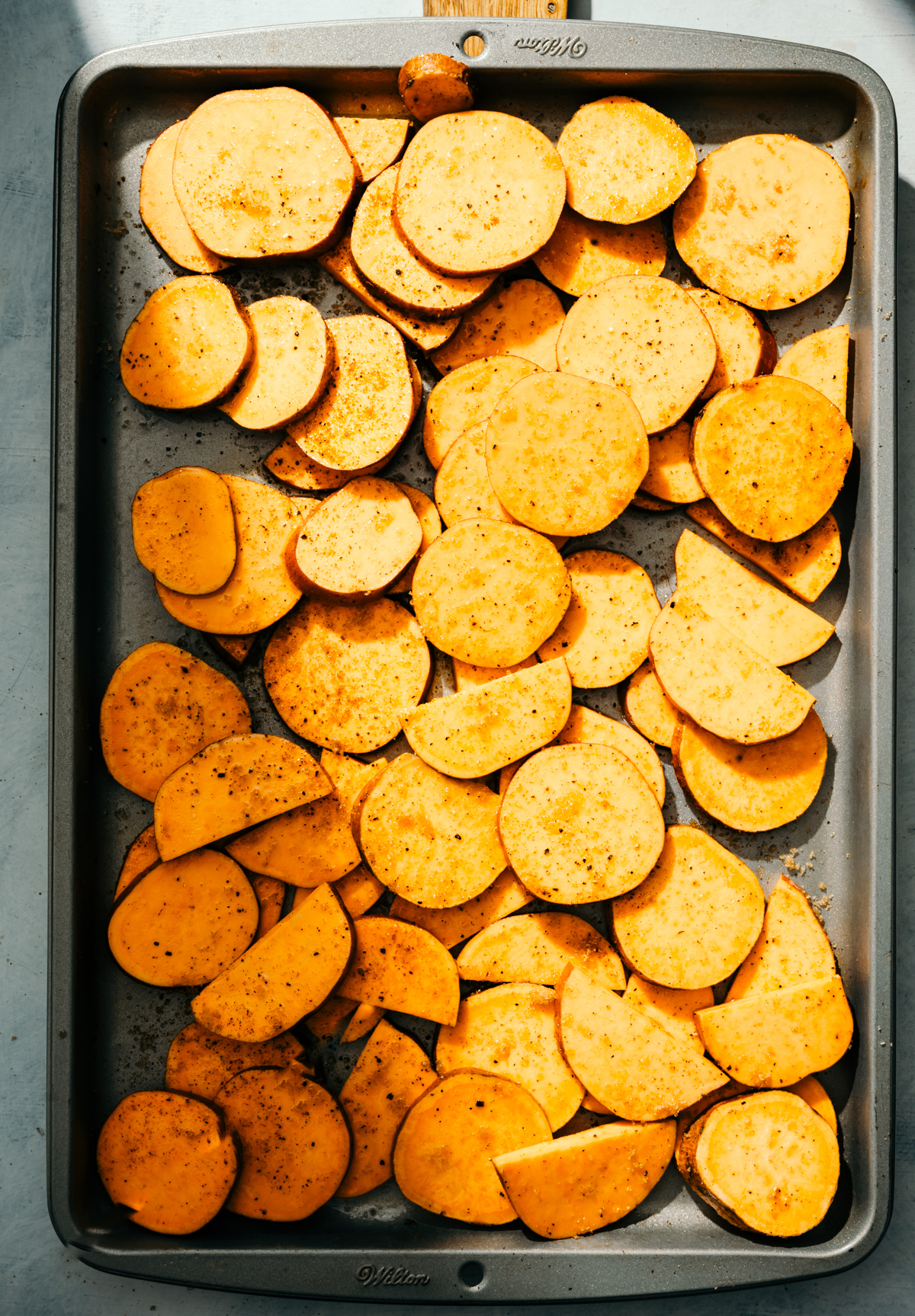 sliced seasoned raw sweet potatoes on a baking sheet