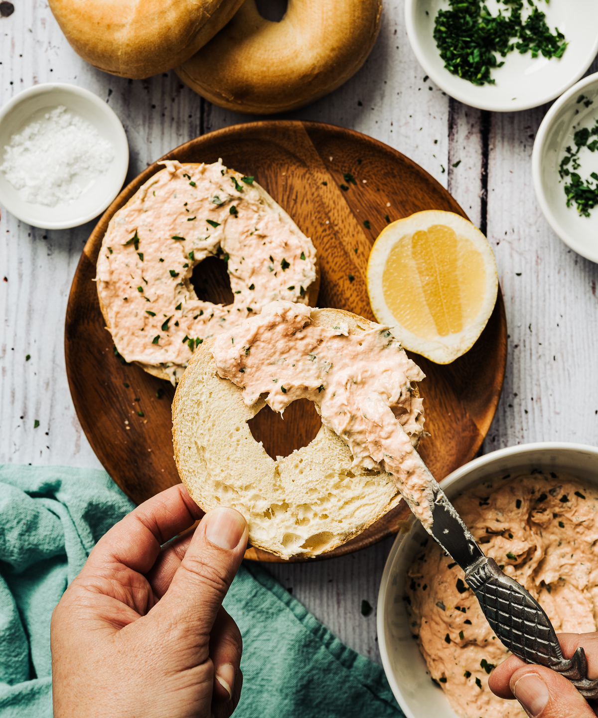 salmon spread being spread on a bagel half, bowl of spread another bagel half spread with smoked salmon lemon slice