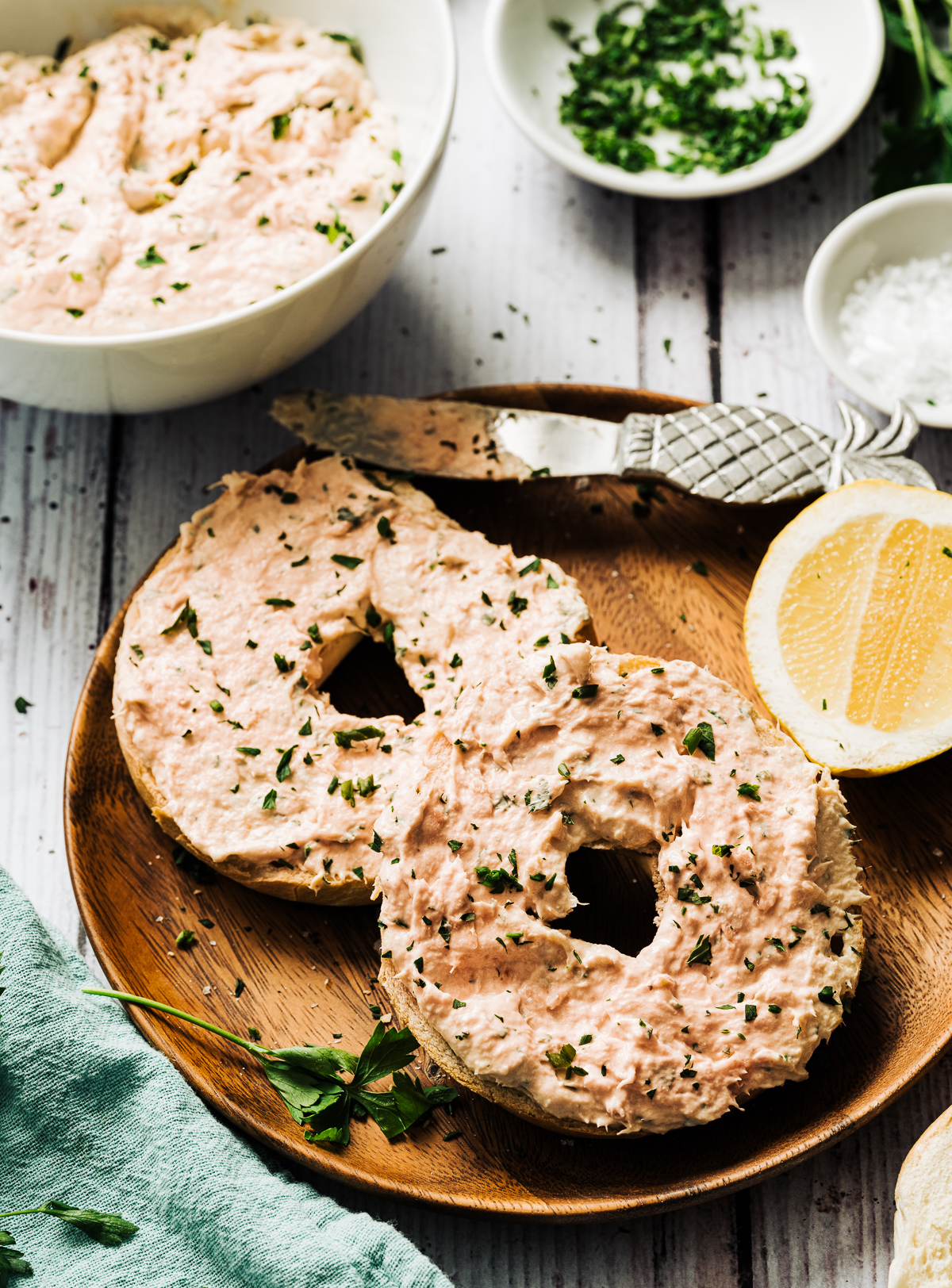 smoked salmon spread on bagel halves on wood plate lemon slice bowl of salmon spread