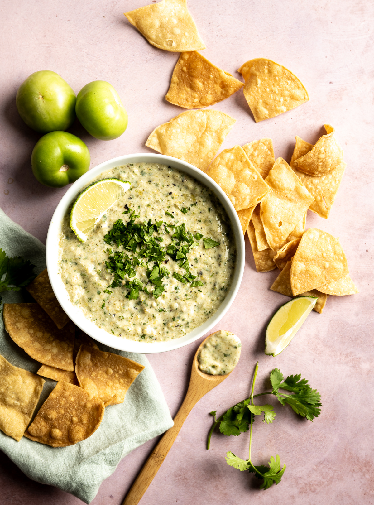 bowl of green salsa with cilantro limes chips wooden spoon green napkin