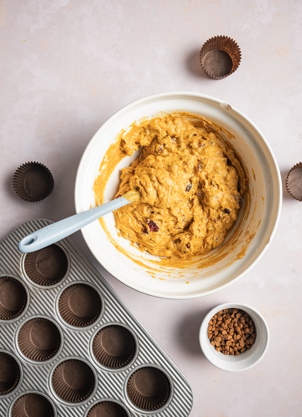 pumpkin muffin batter in a bowl small bowl of cinnamon chips muffin tin with brown liners